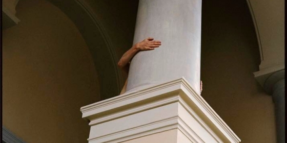 Vi ser en enslig hånd gripe rundt en av museets søyler. I mørket bak skimter vi en kropp.