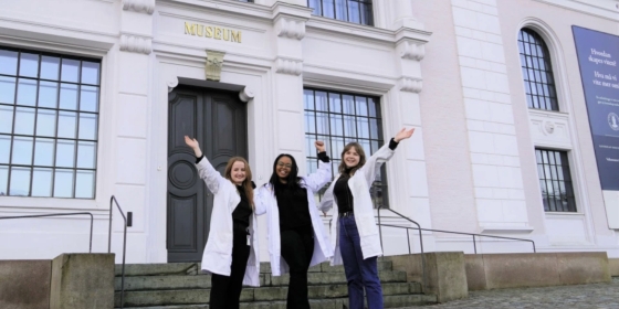 Tre kvinner jubler og rekker hendene i været foran Universitetmuseet, Naturhistorie