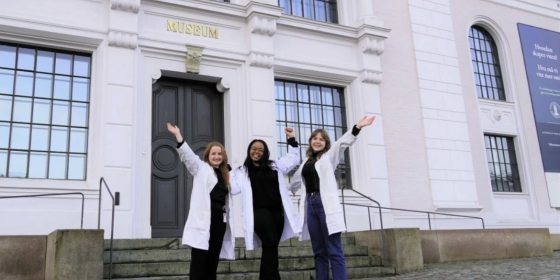 Tre kvinner jubler og rekker hendene i været foran Universitetmuseet, Naturhistorie