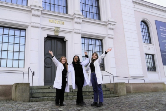 Tre kvinner jubler og rekker hendene i været foran Universitetmuseet, Naturhistorie